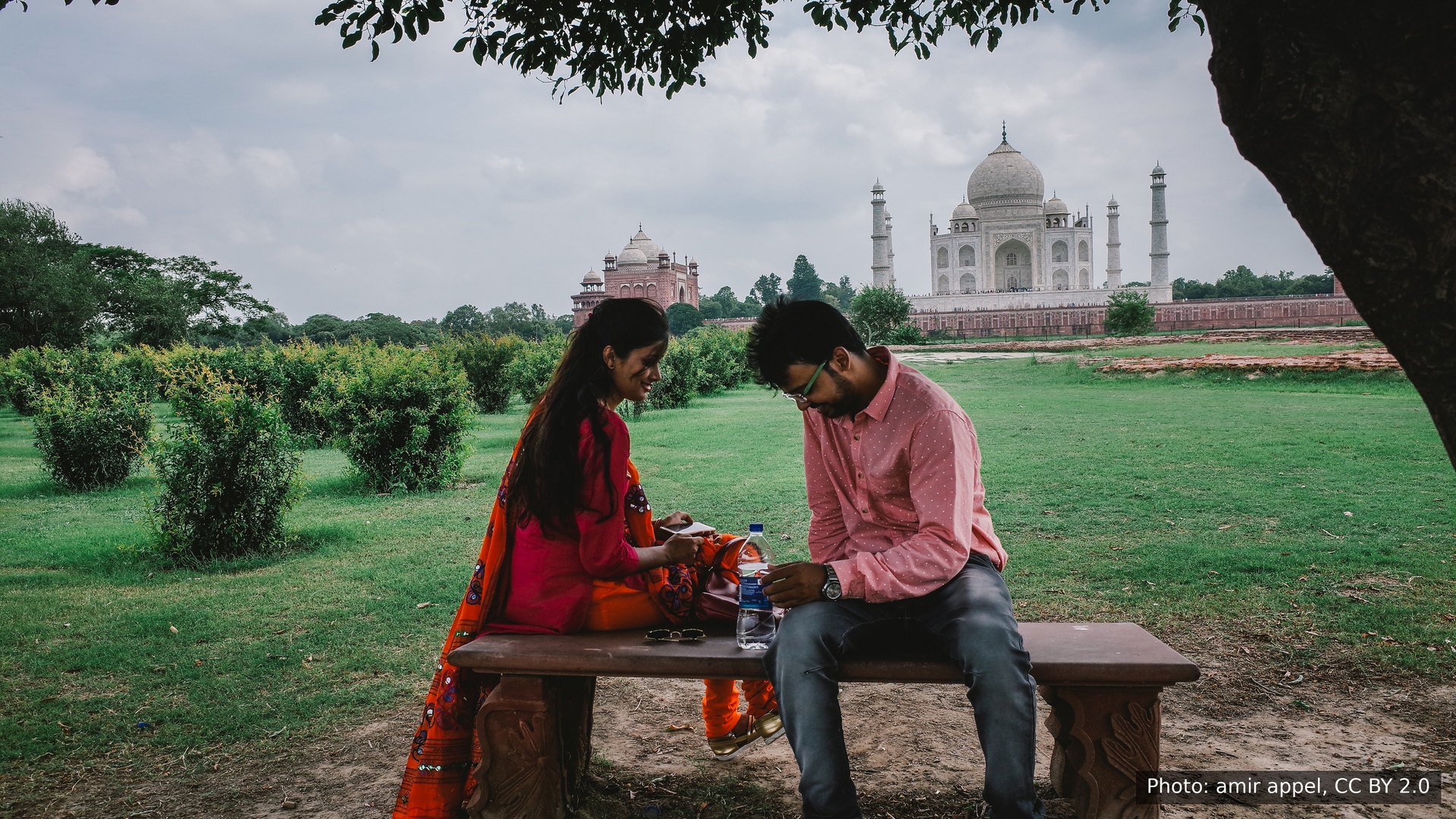A young couple on a bench in the gardens facing the Taj Mahal