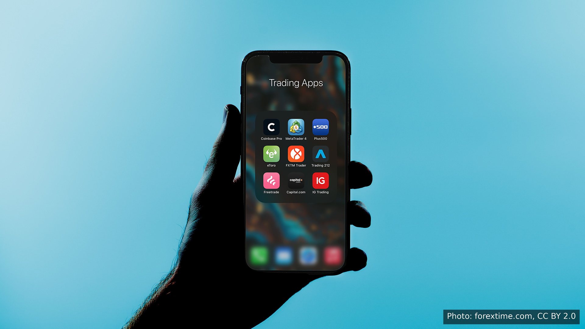 A hand holding a phone with trading apps, in silhouette